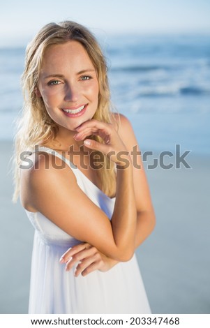 Pretty blonde standing at the beach in white sundress smiling at camera on a sunny day