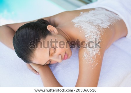 Calm brunette lying on towel with salt treatment on back outside at the spa
