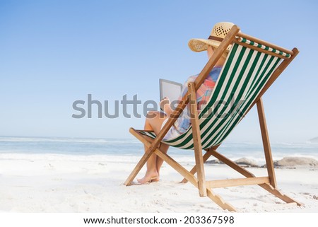 Woman in sunhat sitting on beach in deck chair using tablet pc on a sunny day