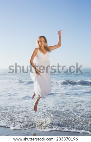Pretty blonde jumping at the beach in white sundress on a sunny day
