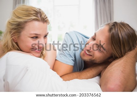 Happy couple relaxing on bed smiling at each other at home in the bedroom