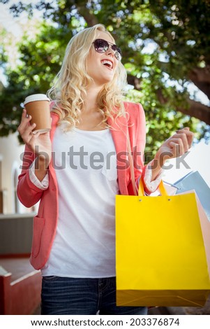 Pretty blonde holding shopping bags and coffee cup on a sunny day in the city