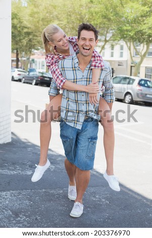 Young hip man giving his blonde girlfriend a piggy back on a sunny day in the city