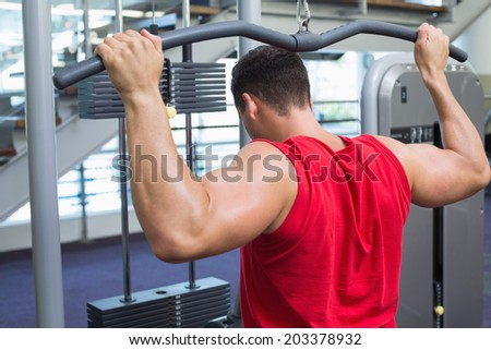 Strong bodybuilder using weight machine for arms at the gym