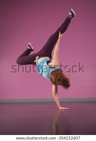 Pretty break dancer doing handstand with one hand in the dance studio