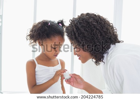 Pretty mother showing her daughter face cream at home in the bathroom