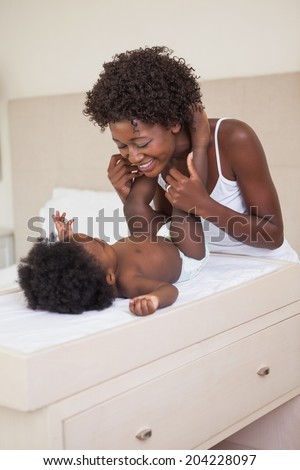 Happy mother with baby girl on changing table at home in the bedroom