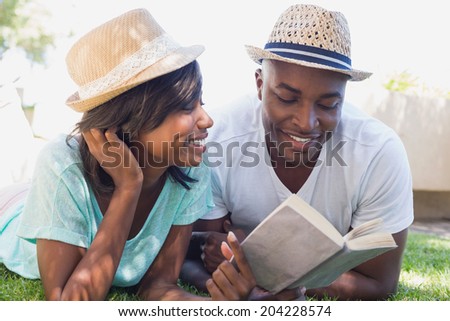 Happy couple lying in garden together reading book on a sunny day