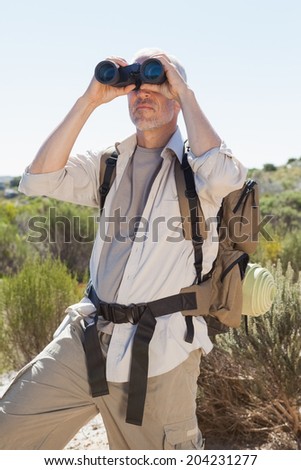 Hiker looking through binoculars on country trail on a sunny day