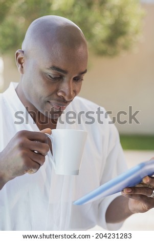Handsome man in bathrobe using tablet at breakfast outside on a sunny day