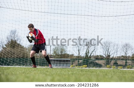 Goalkeeper in red saving a goal during a game on a clear day
