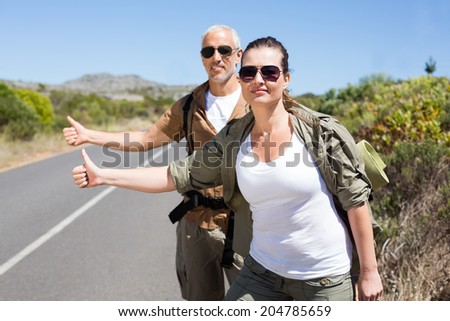 Hitch hiking couple standing on the side of the road with thumb out on a sunny day