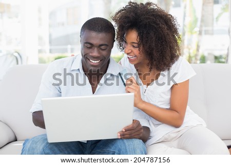 Attractive couple using laptop together on sofa to shop online at home in the living room