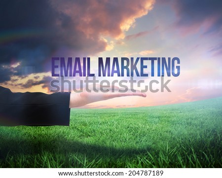 Businesswomans hand presenting the words email marketing against green field under orange sky