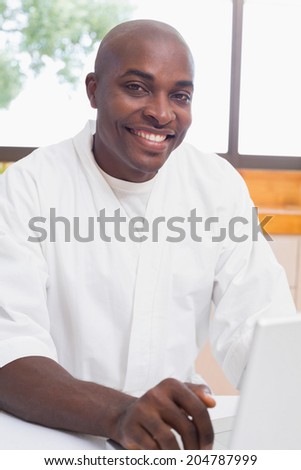 Happy man in bathrobe using laptop at table at home in the kitchen