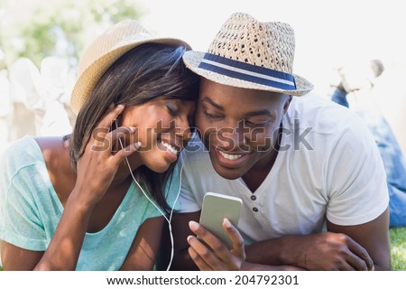 Happy couple lying in garden together listening to music on a sunny day