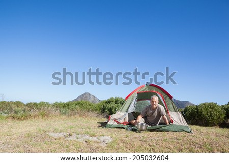 Happy camper cooking on camping stove outside his tent on a sunny day