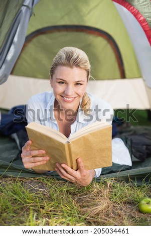 Attractive happy blonde lying in tent holding book on a sunny day