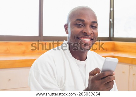 Happy man in bathrobe sending a text at home in the kitchen