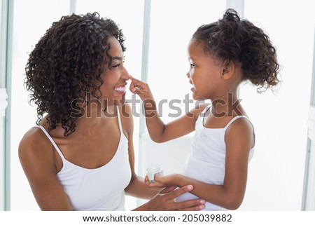 Cute daughter putting face cream on mothers nose at home in the bathroom
