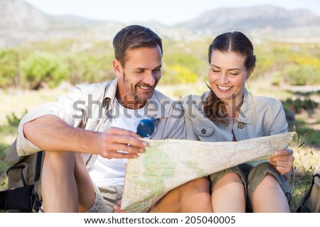 Happy hiking couple reading the map on mountain trail on a sunny day