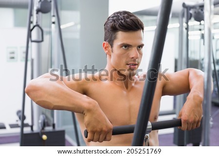Portrait of a shirtless young muscular man using biceps pull up in gym