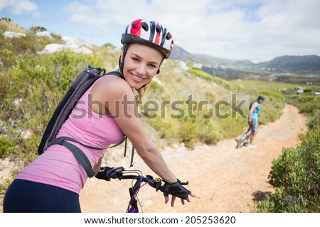 Fit couple cycling on mountain trail woman smiling at camera on a sunny day
