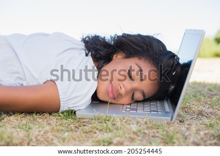 Casual pretty woman lying on the grass sleeping on her laptop on a sunny day in the countryside