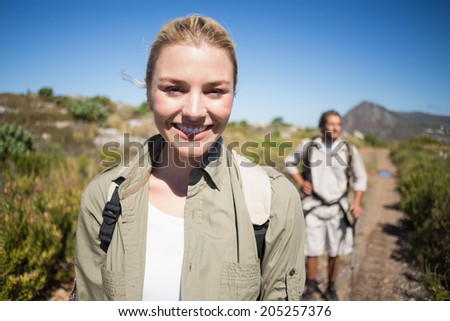 Hiking couple walking on mountain terrain woman smiling at camera on a sunny day