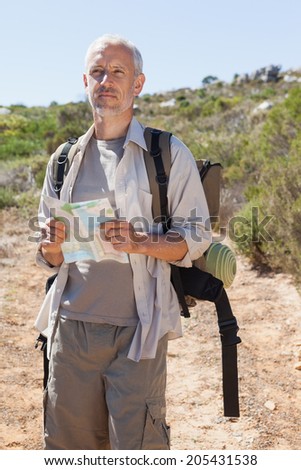 Handsome hiker consulting the map in the countryside on a sunny day