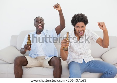 Football fans cheering holding beer bottles at home in the living room