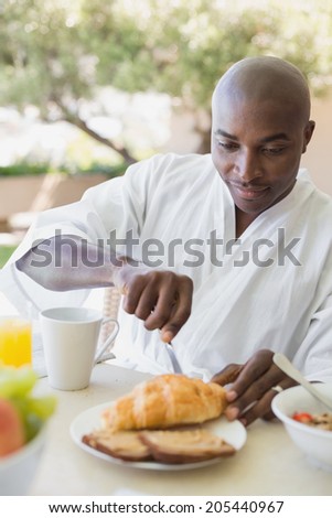 Handsome man in bathrobe having breakfast outside on a sunny day