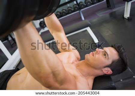 Shirtless young muscular man exercising with dumbbells in gym