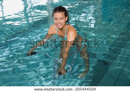 Fit brunette using underwater exercise bike in swimming pool at the leisure centre