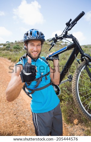 Fit man walking down trail holding mountain bike smiling at camera on a sunny day