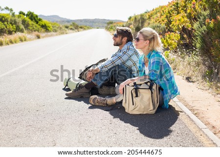 Attractive couple sitting on the road waiting for a lift on a sunny day