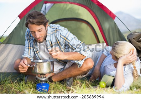 Attractive happy couple cooking on camping stove on a sunny day