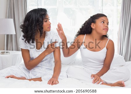 Mother and daughter having an argument on bed at home in bedroom