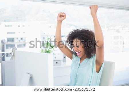 Casual businesswoman cheering at her desk in her office