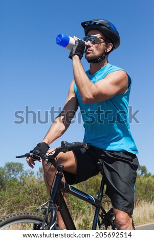 Handsome cyclist taking a break on his bike drinking water on a sunny day