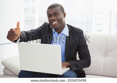 Happy businessman sitting on couch with laptop showing thumbs up at home in the living room