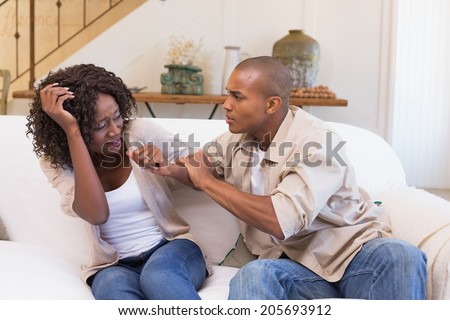 Angry man grabbing his scared partner on sofa at home in the living room