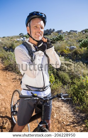 Fit cyclist adjusting helmet strap on country terrain smiling at camera on a sunny day