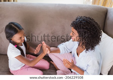 Pretty mother playing clapping game with daughter on couch at home in the living room
