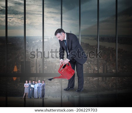 Mature businessman watering tiny business team against room with large window looking on city