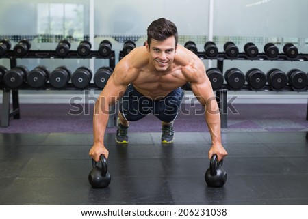 Portrait of a muscular man doing push ups with kettle bells in gym