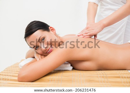 Beautiful brunette enjoying a back massage smiling at camera in the health spa