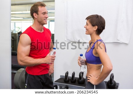 Fit attractive couple chatting holding water bottles at the gym