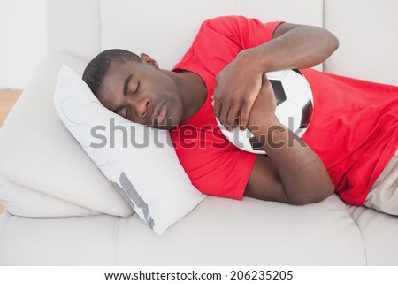 Football fan sleeping on couch hugging ball at home in the living room
