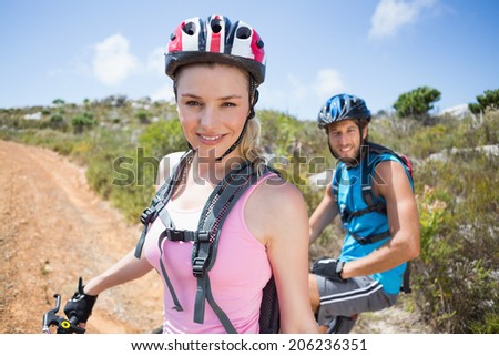 Fit couple cycling up mountain trail smiling at camera on a sunny day